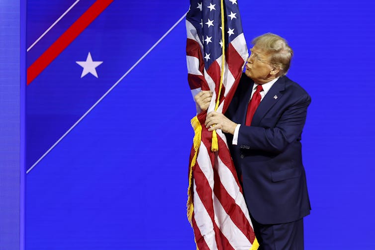 A man dressed in red, white and blue hugging and kissing an American flag.